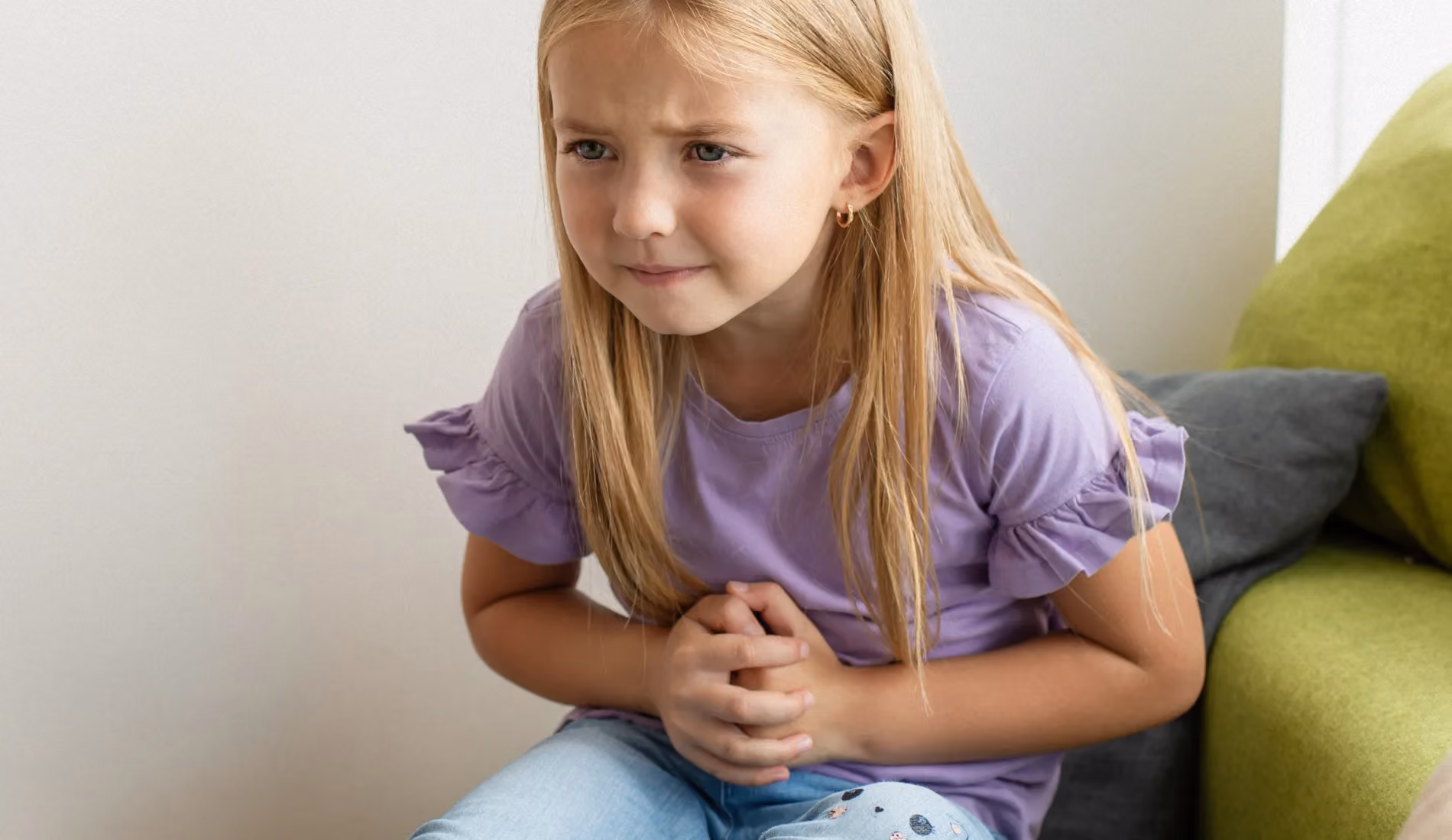 Petite fille courbée en deux, mains crispées sur le ventre, illustrant les maux de ventre récurrents d'un enfant avant d'aller à l'école.