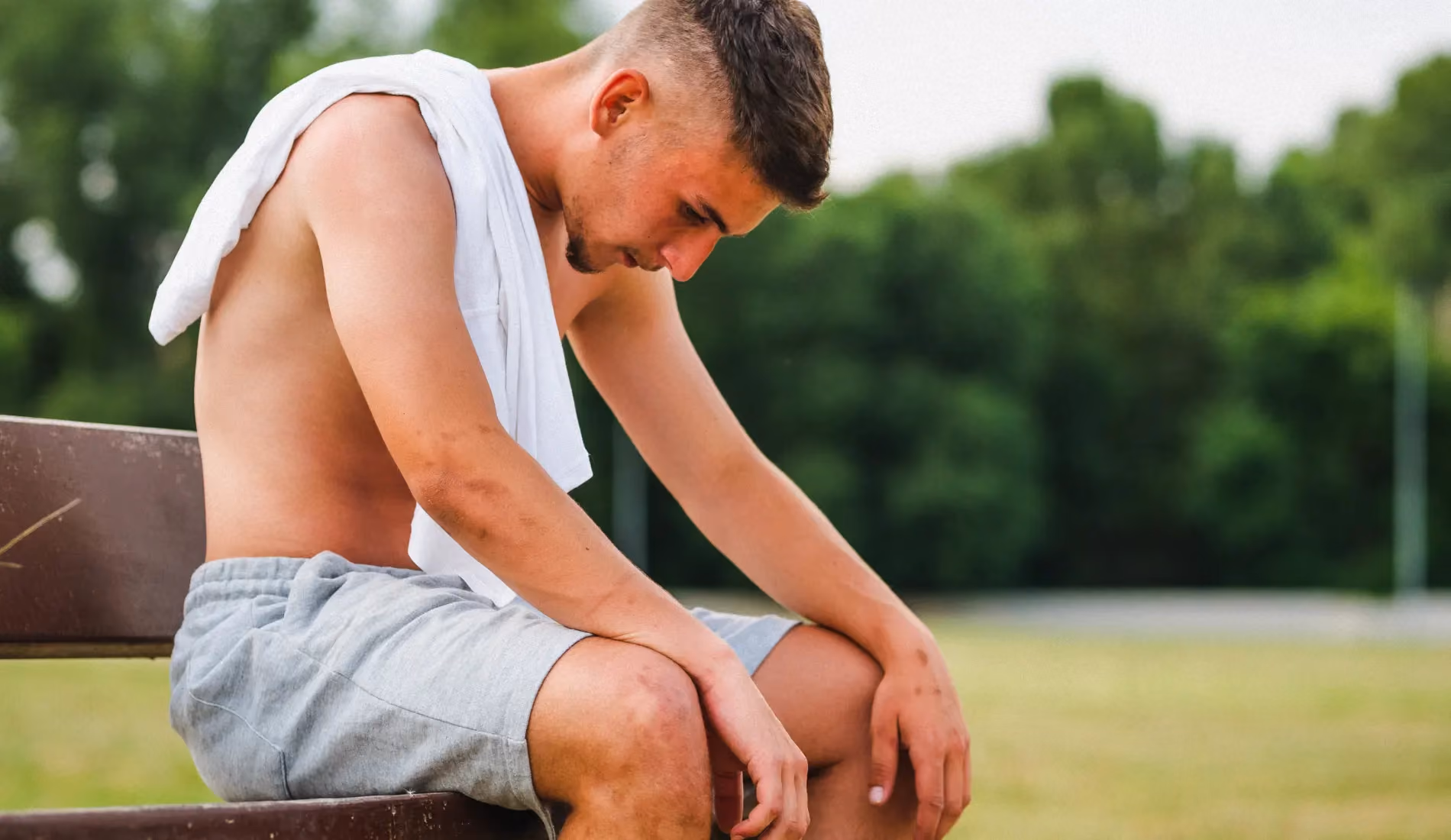 Un jeune sportif assis sur un banc, la tête baissée car il est atteint de pubalgie.