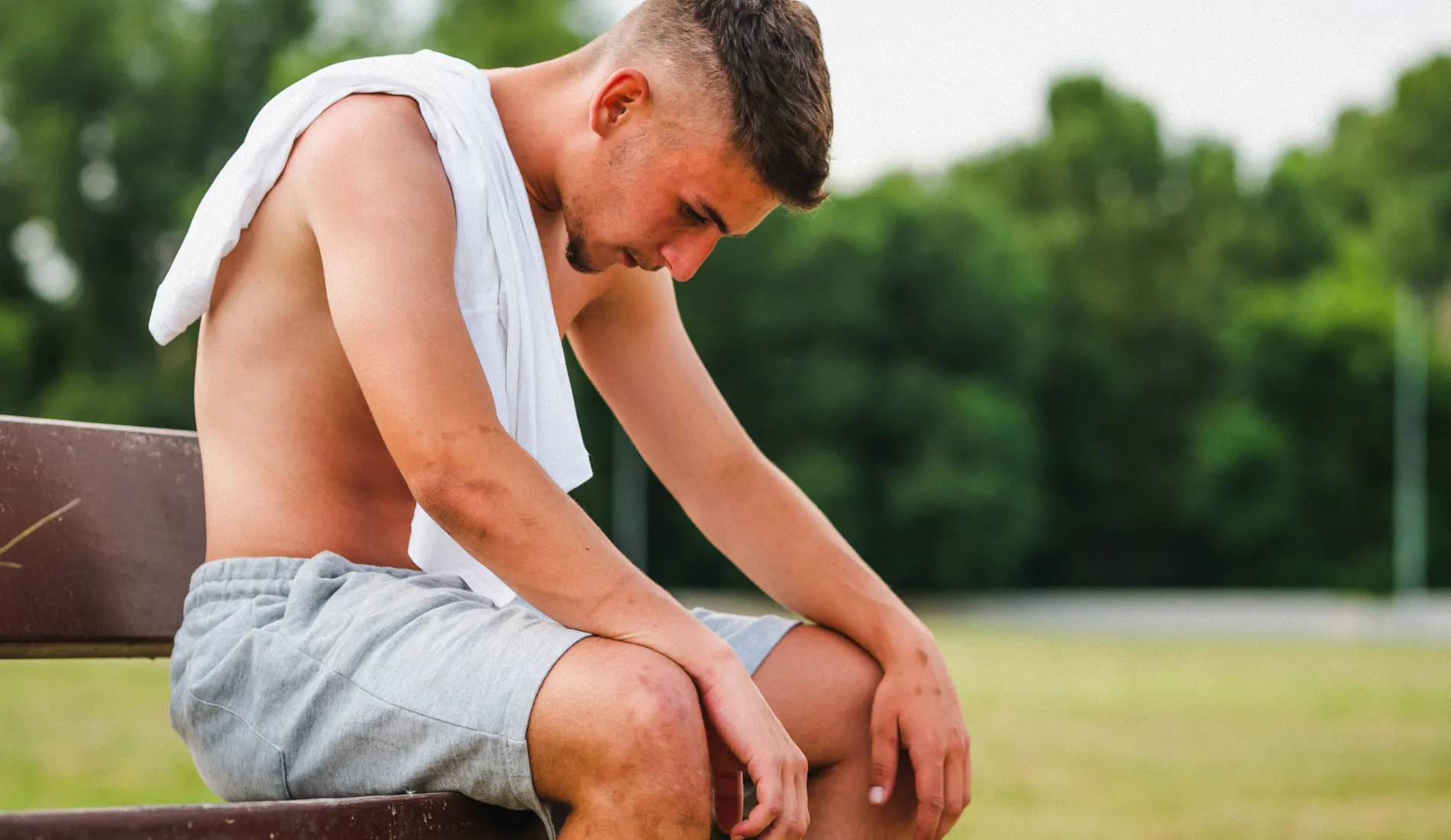 Un jeune sportif assis sur un banc, la tête baissée car il est atteint de pubalgie.