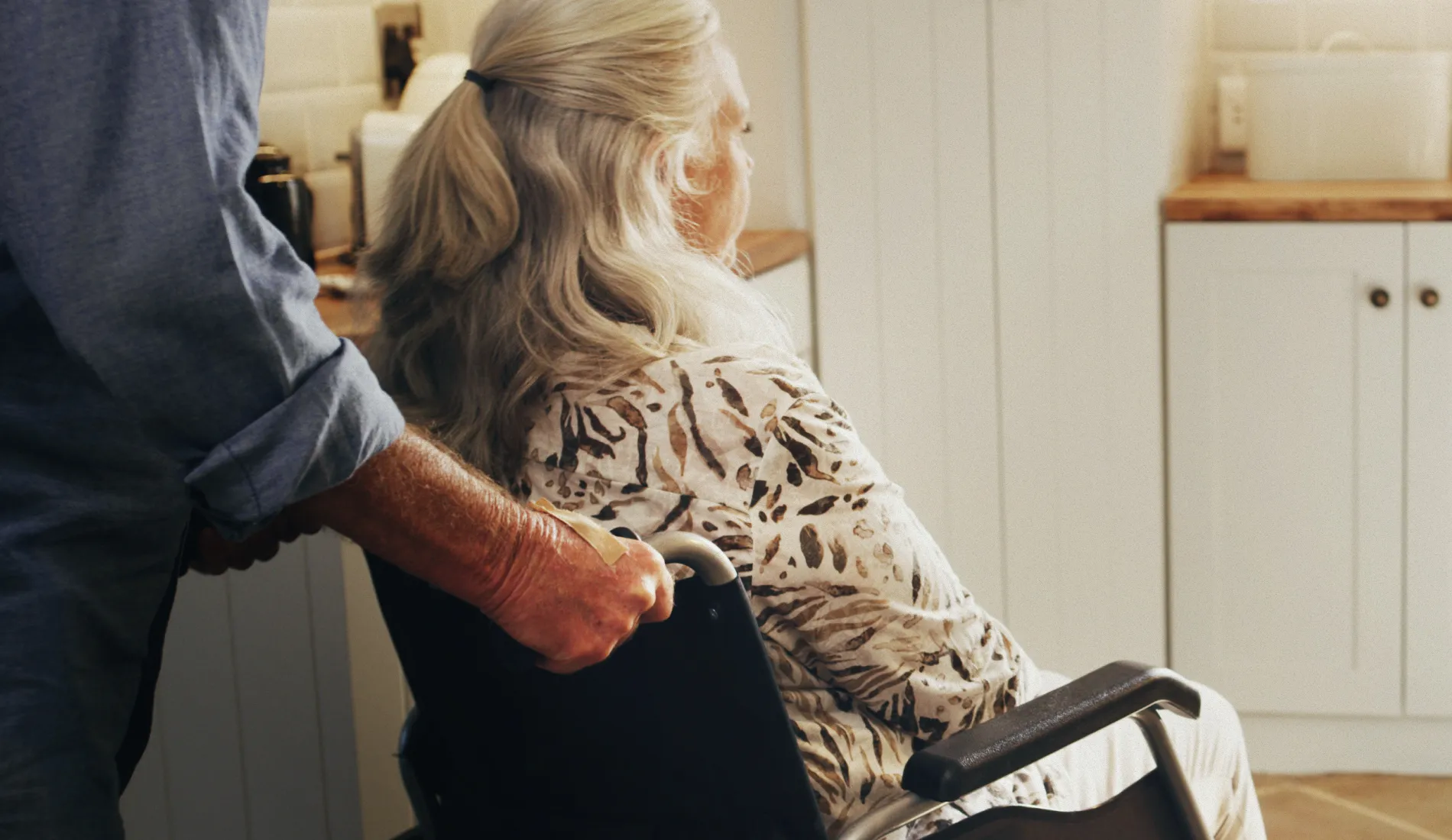 Personne âgée assise dans un fauteuil roulant poussé par une autre personne, signe de la dépendance.