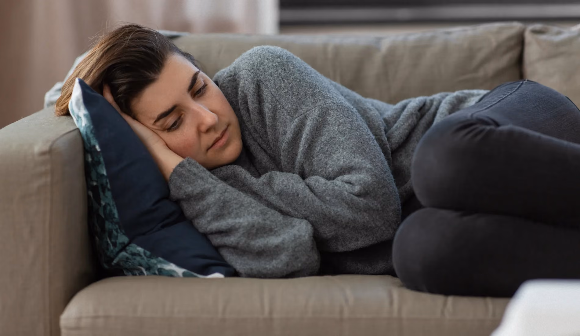 Personne allongée en position repliée sur elle-même dans un canapé, illustrant les contractures musculaires involontaires et la raideur caractéristiques de la spasticité