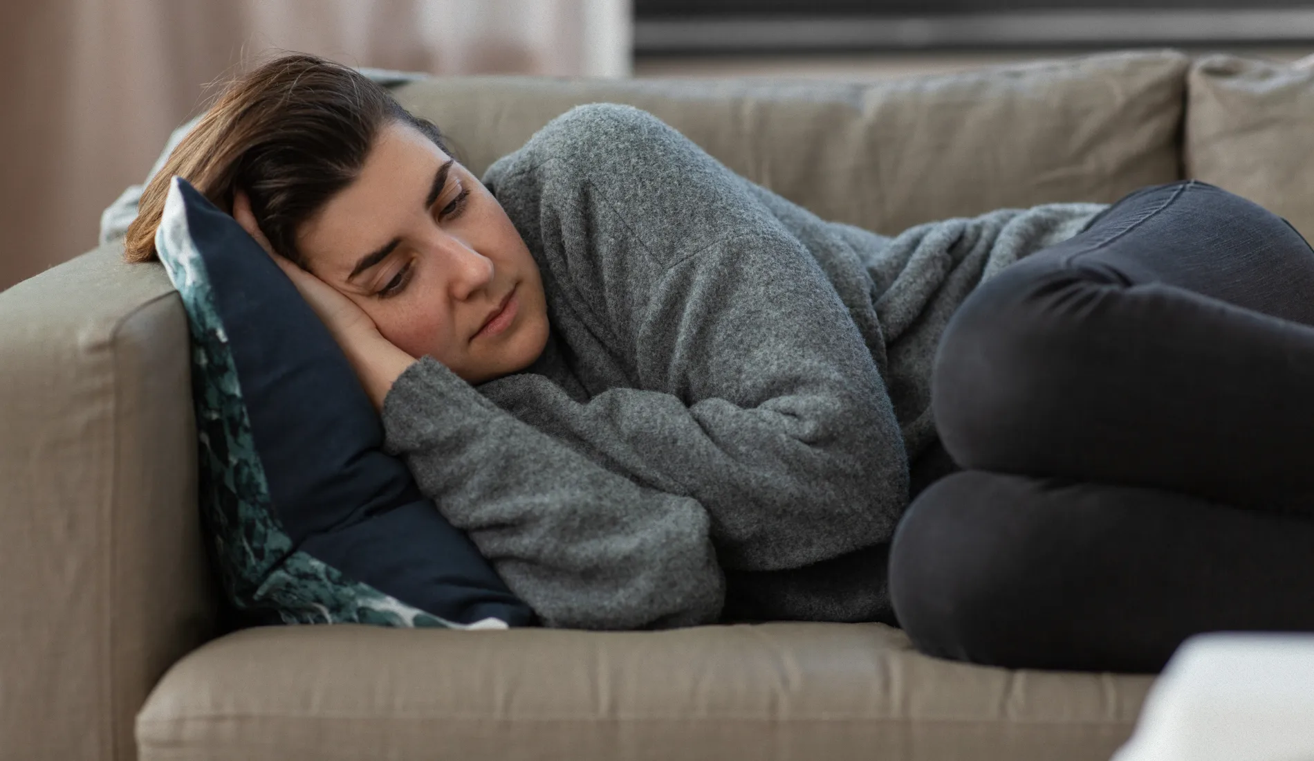 Personne allongée en position repliée sur elle-même dans un canapé, illustrant les contractures musculaires involontaires et la raideur caractéristiques de la spasticité