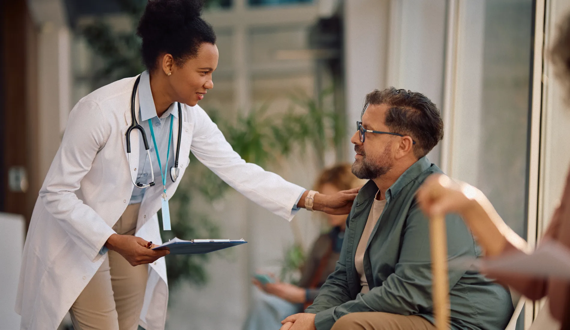 Médecin debout la main posée sur l'épaule d'un patient assis, illustrant la relation de confiance au cœur de l'éducation à la santé.