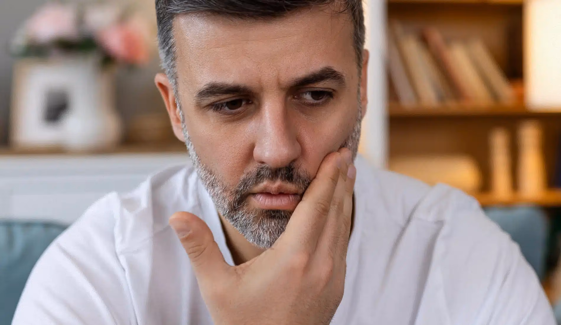 Une personne à l'air anxieux qui se touche sa joue, signe d'un abcès dentaire.