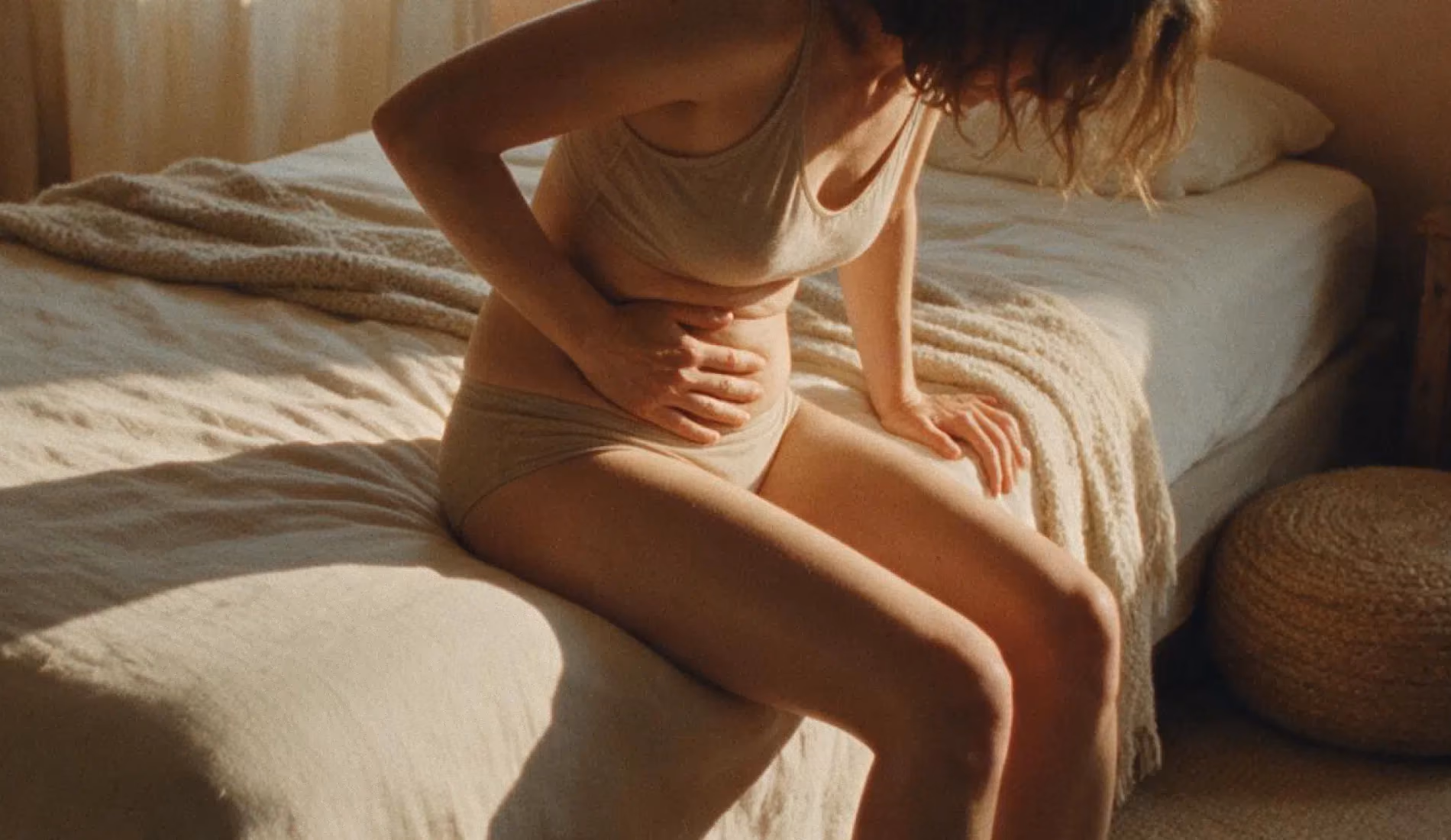 Une personne assise au bord du lit, tenant son ventre car elle souffre de chlamydia
