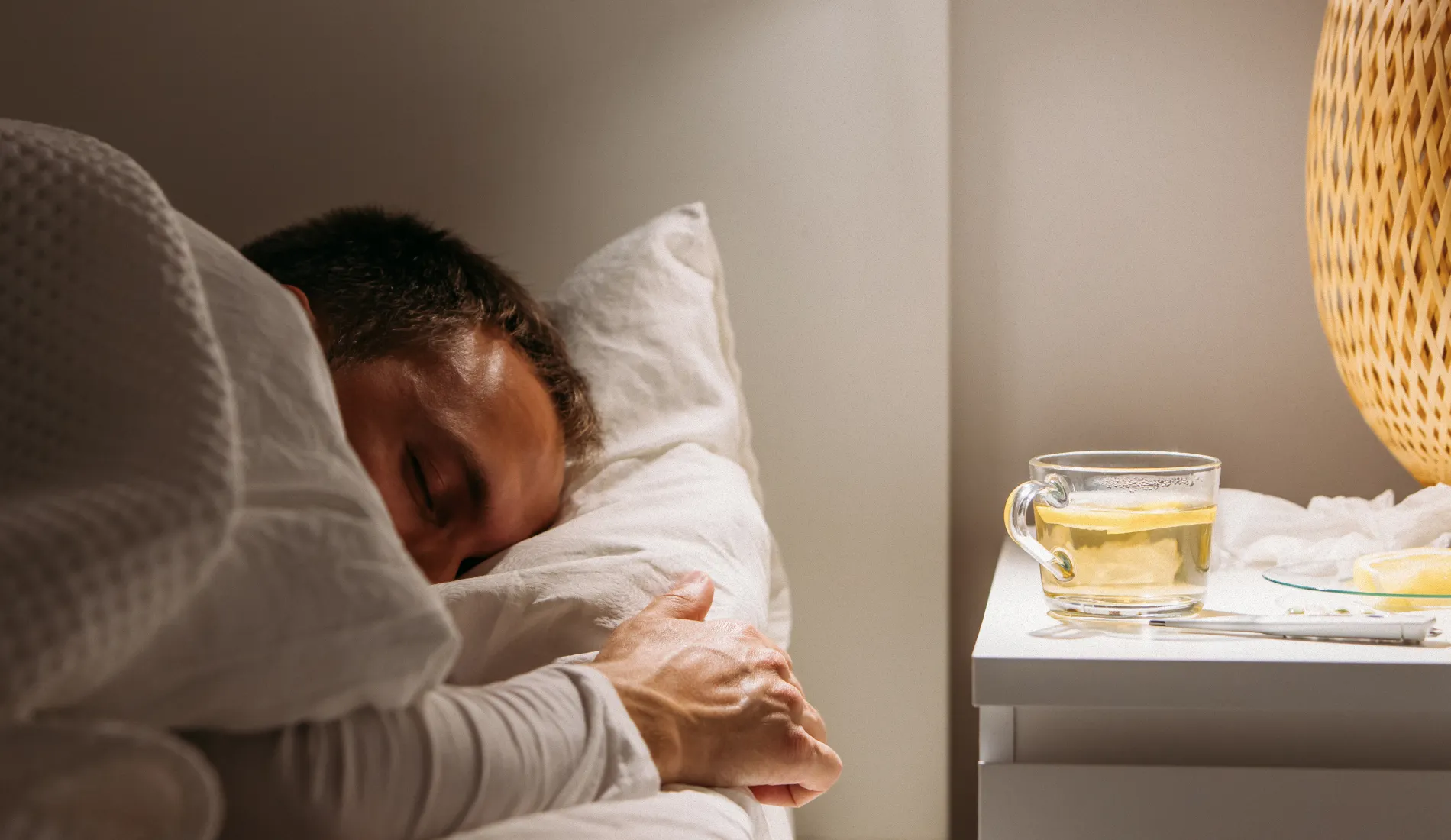 Une personne allongée dans un lit, les yeux fermés, l'air pâle à cause de la fièvre liée aux symptômes de la grippe.