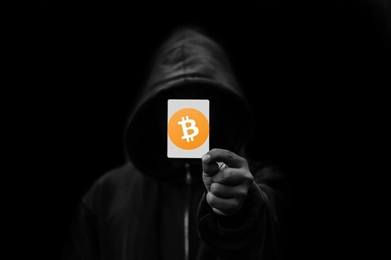 Homem não identificado em um lugar escuro segura uma carta com o símbolo do Bitcoin