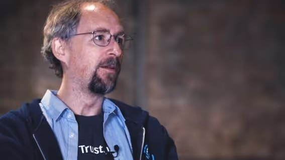 Homem branco de cabelos grisalhos usando óculos de grau e moletom cinza de perfil