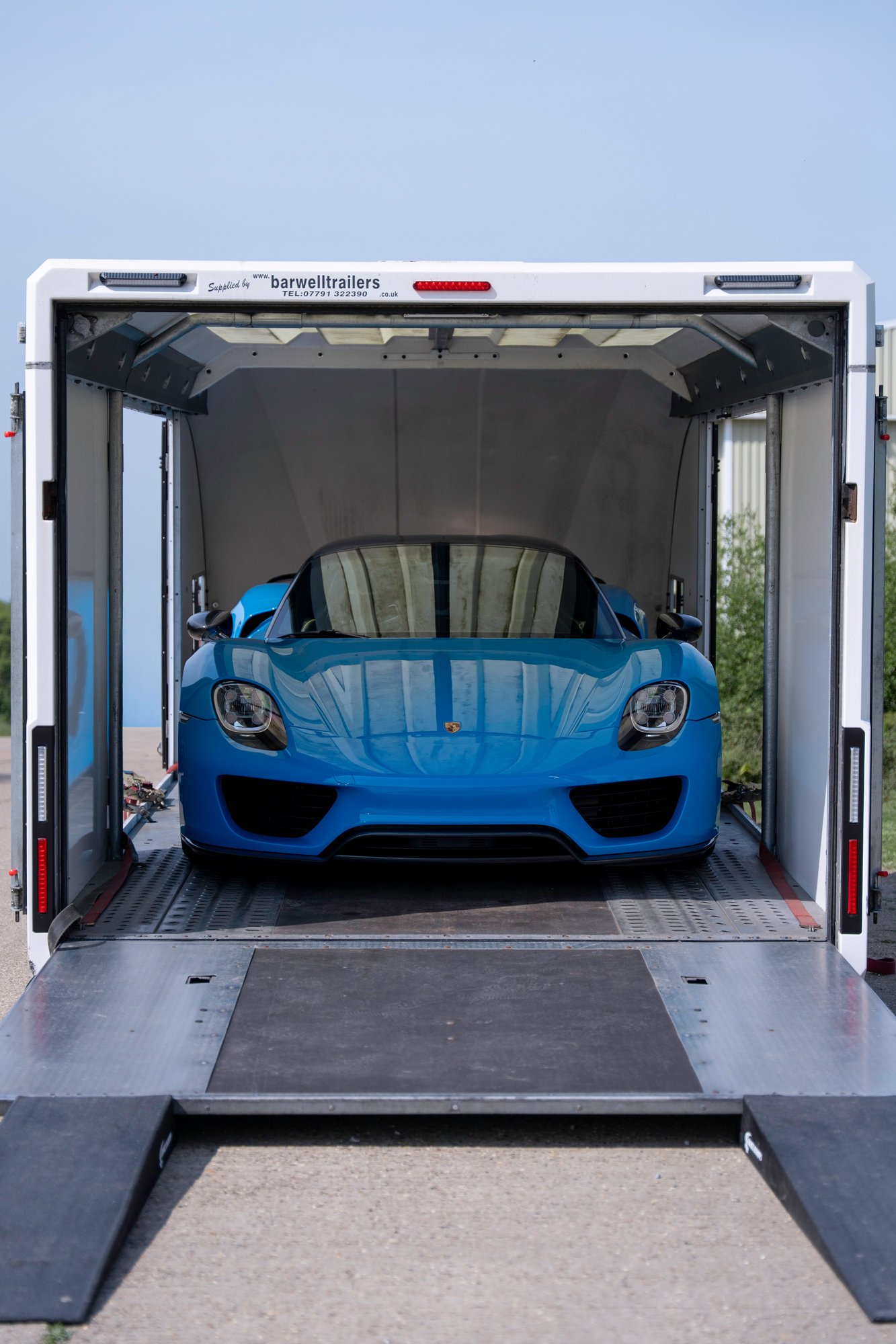 Porsche 918 Spyder viewed head-on inside an enclosed car transporter with ramps lowered