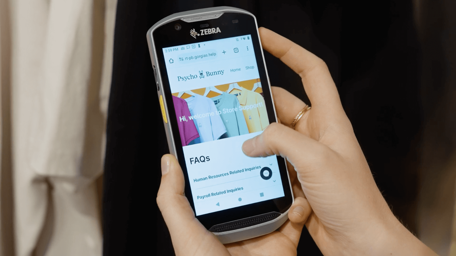 Hand holding a Zebra mobile device displaying the Psycho Bunny store support site with FAQ options.