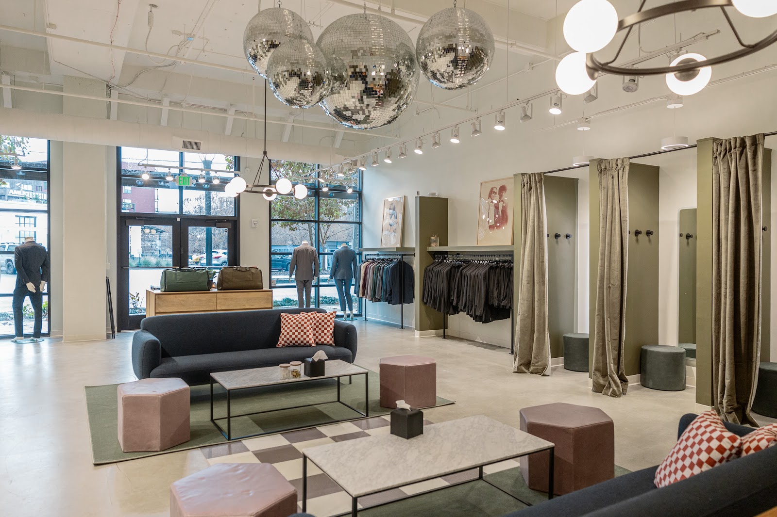 SuitShop showroom with fitting rooms, hanging suits, display mannequins, large windows, lounge seating, and decorative disco balls.