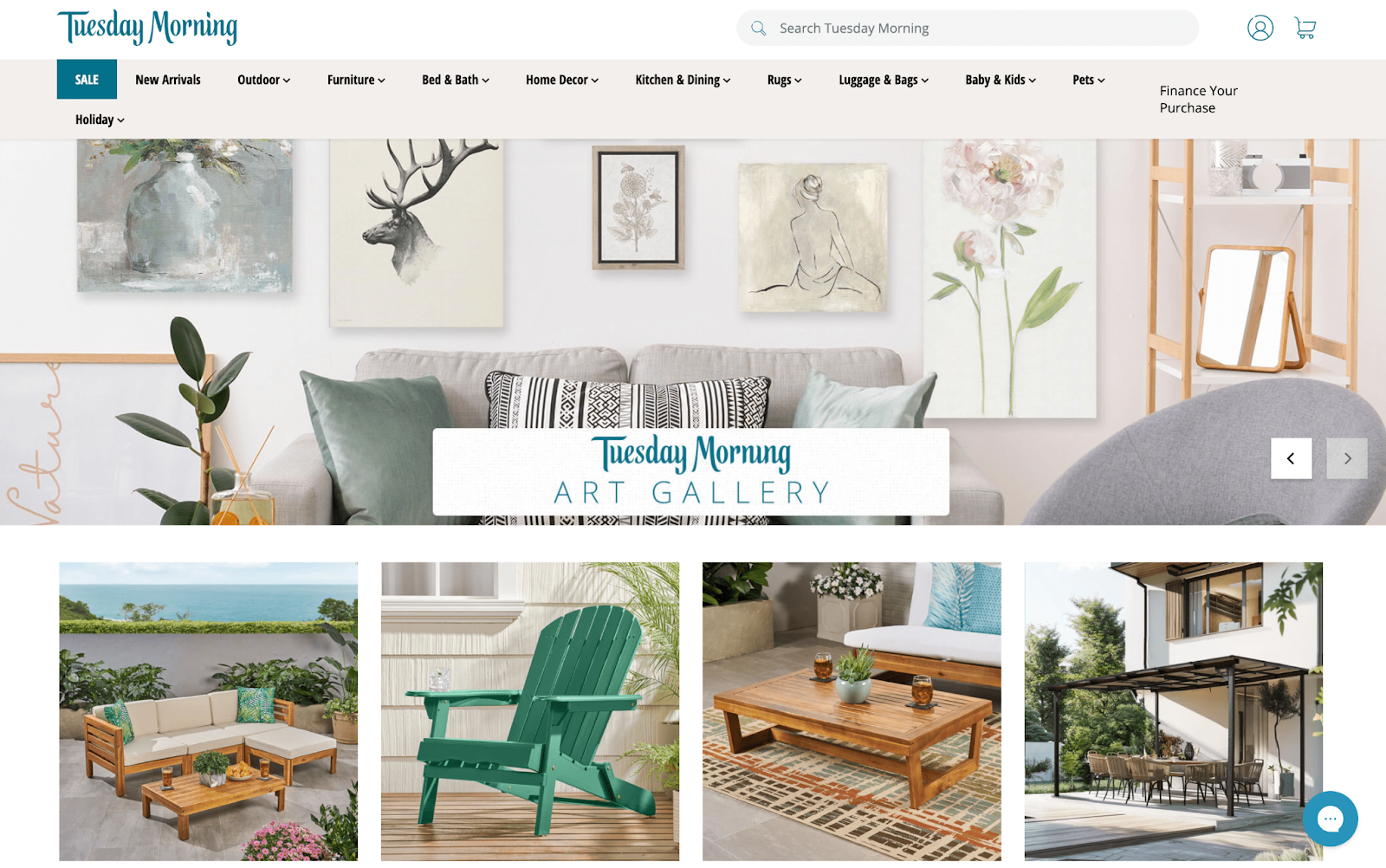 Tuesday Morning homepage showing navigation menu and featured product images including wall art, outdoor seating, and wooden furniture.