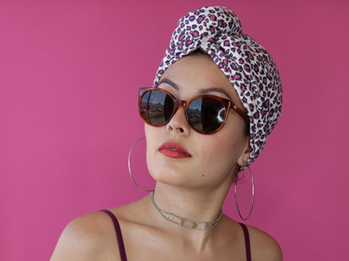 A woman wears a leopard print towel turban with sunglasses on a hot pink background.