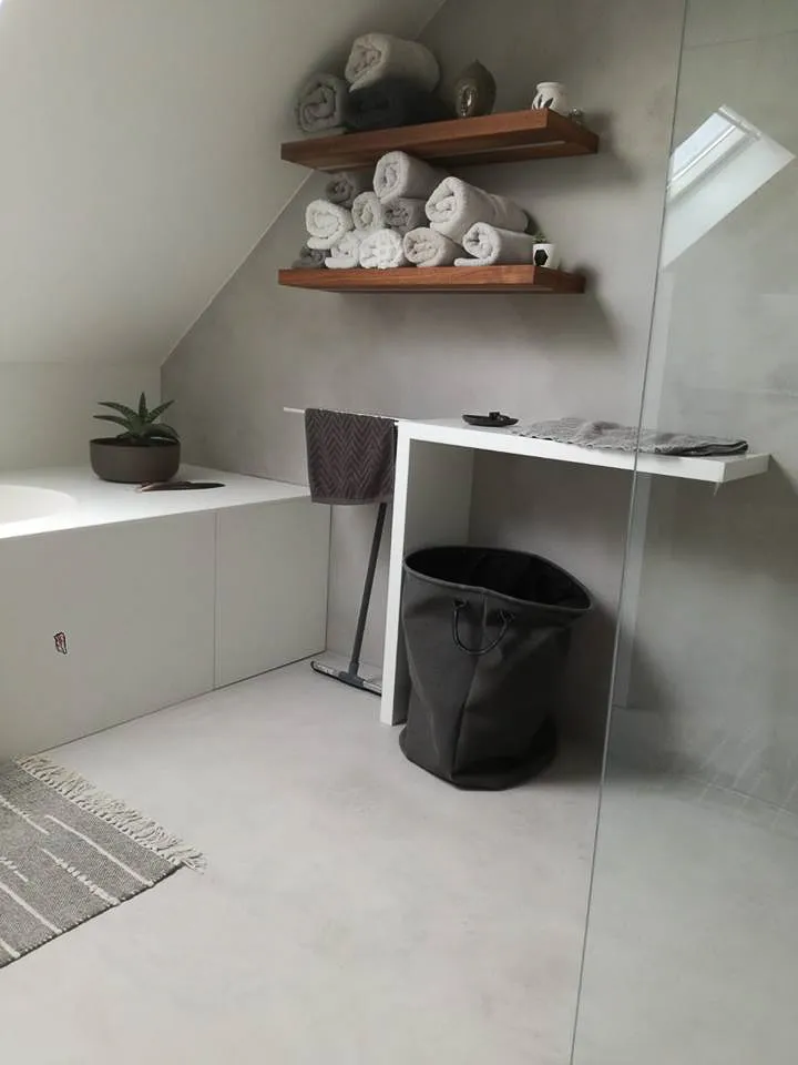 Light grey microcement bathroom floor and walls under a sloping ceiling with wooden shelves