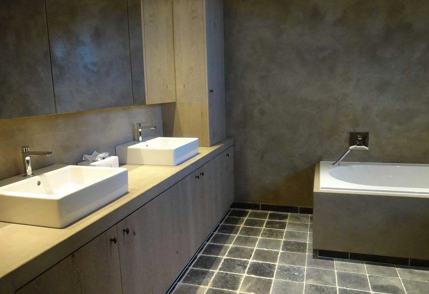 Bathroom with grey microcement walls and bath surround, double-basin vanity and slate floor