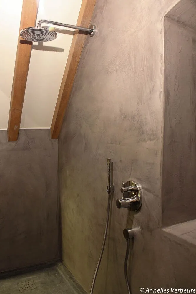 Grey microcement shower under sloping timber beams with built-in niche
