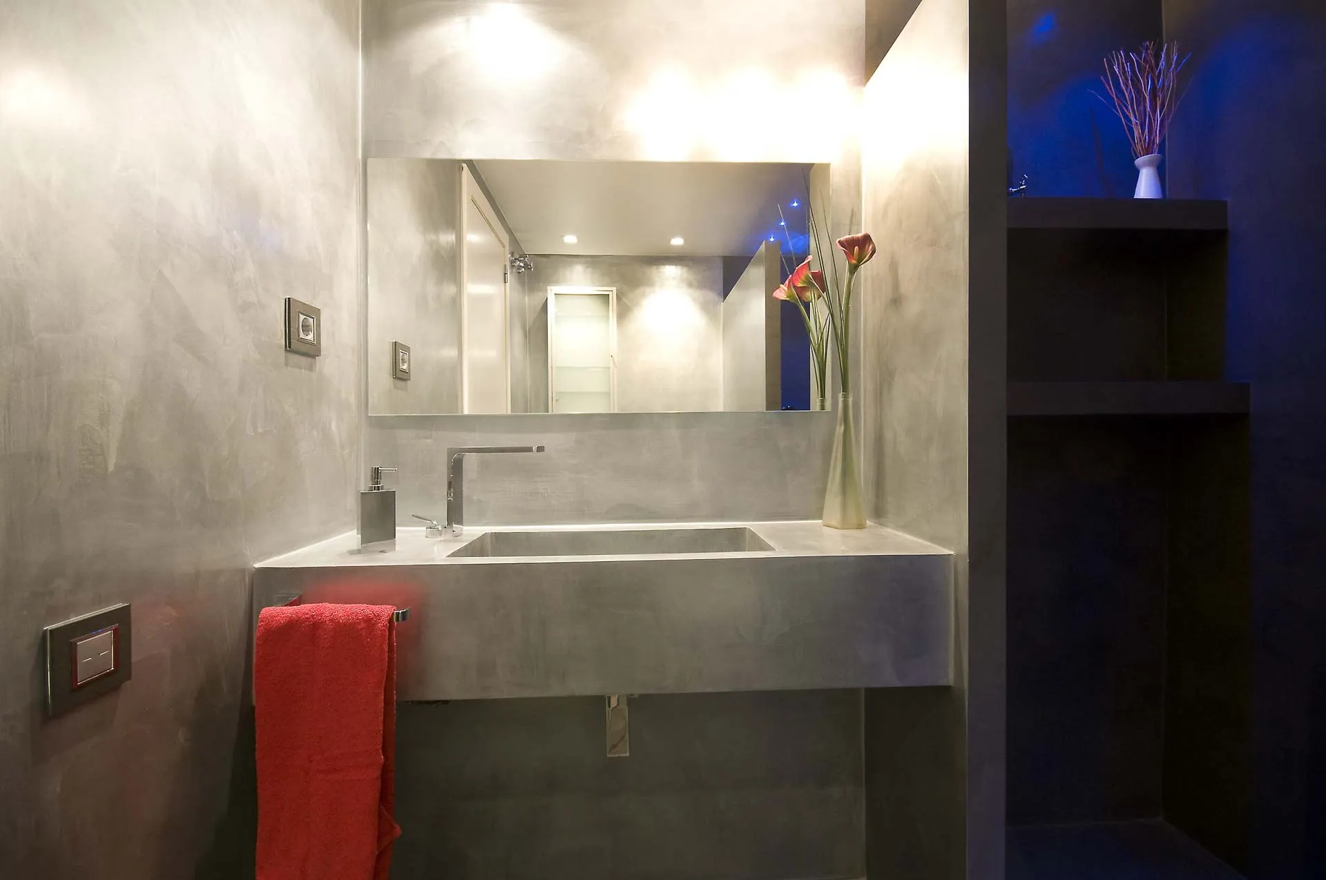 Grey microcement cloakroom with integrated basin, mirror and red towel