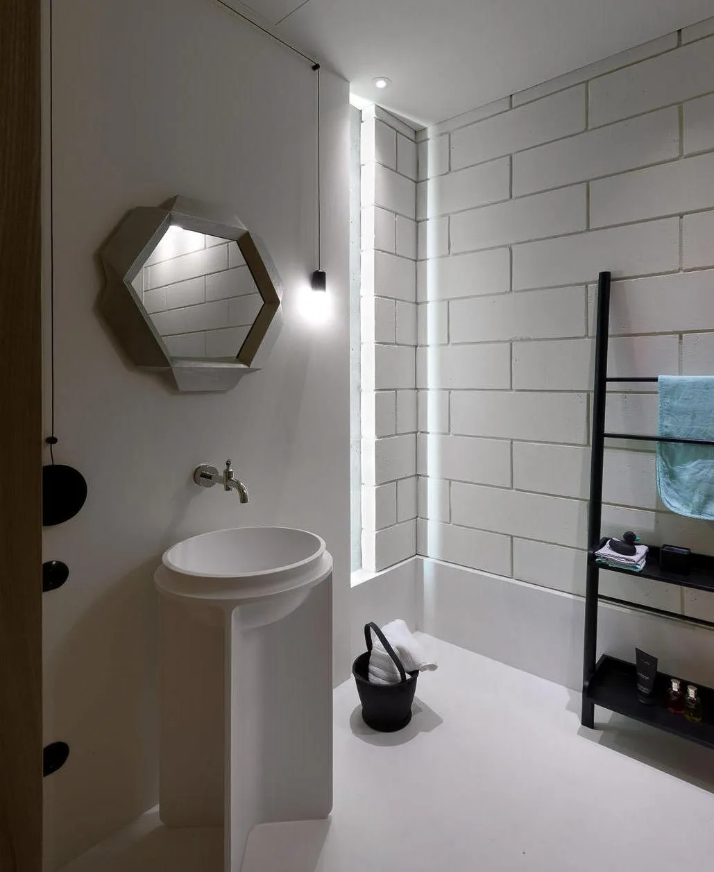 White microcement bathroom floor with pedestal basin and hexagonal mirror