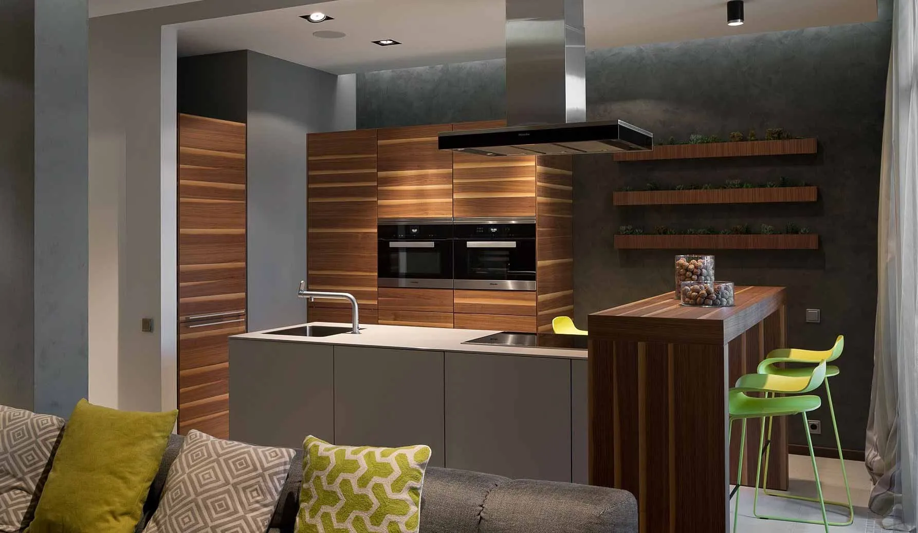 Kitchen with grey microcement walls and island, wood-panelled units and breakfast bar