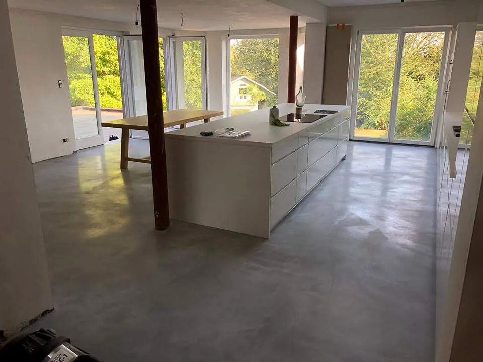 Open-plan kitchen with seamless grey microcement floor and white island