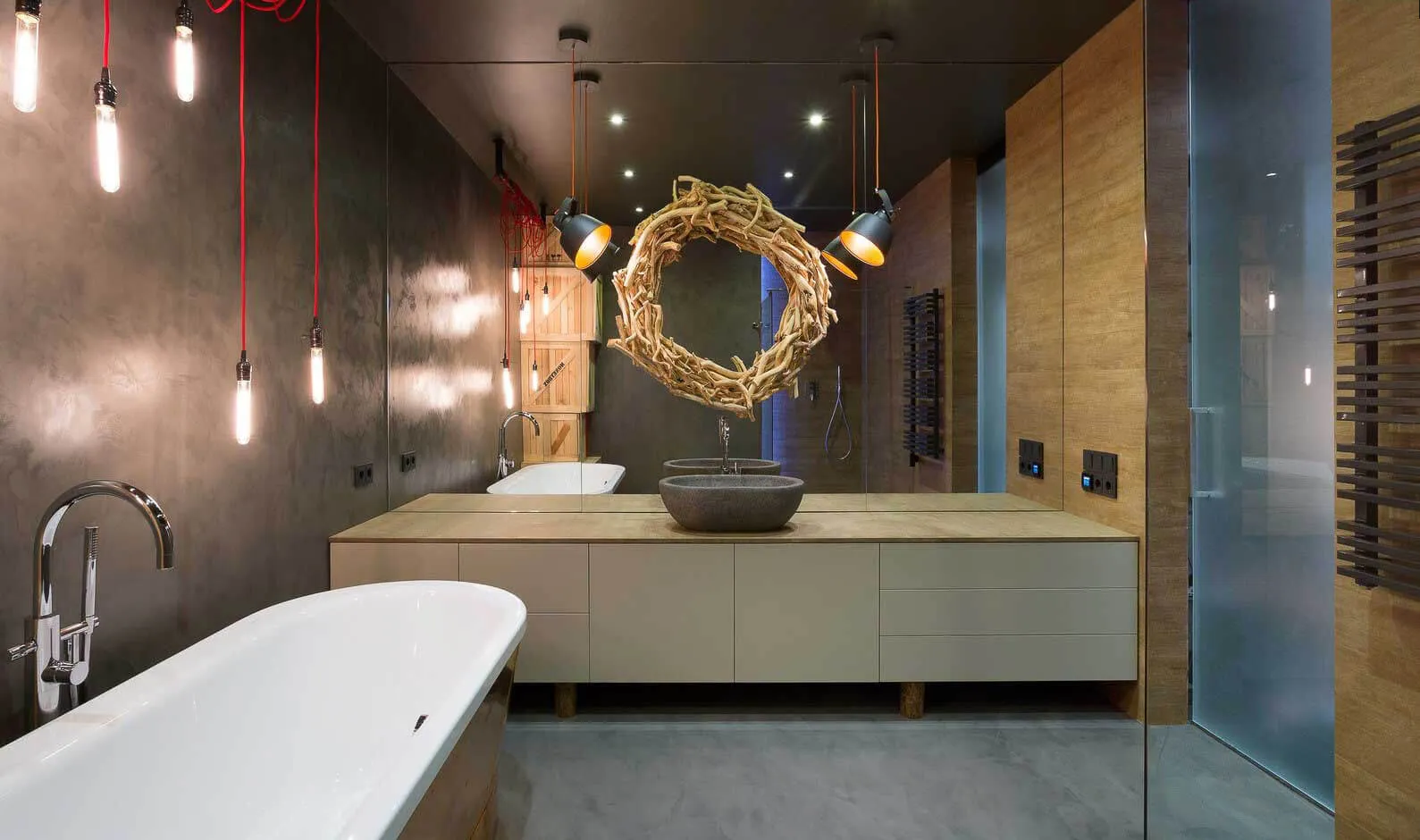 Dark microcement bathroom with freestanding bath, timber vanity, vessel sink and pendant bulbs