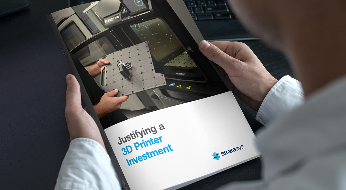 Hands holding the cover of a Stratasys whitepaper, showing a 3D printer.