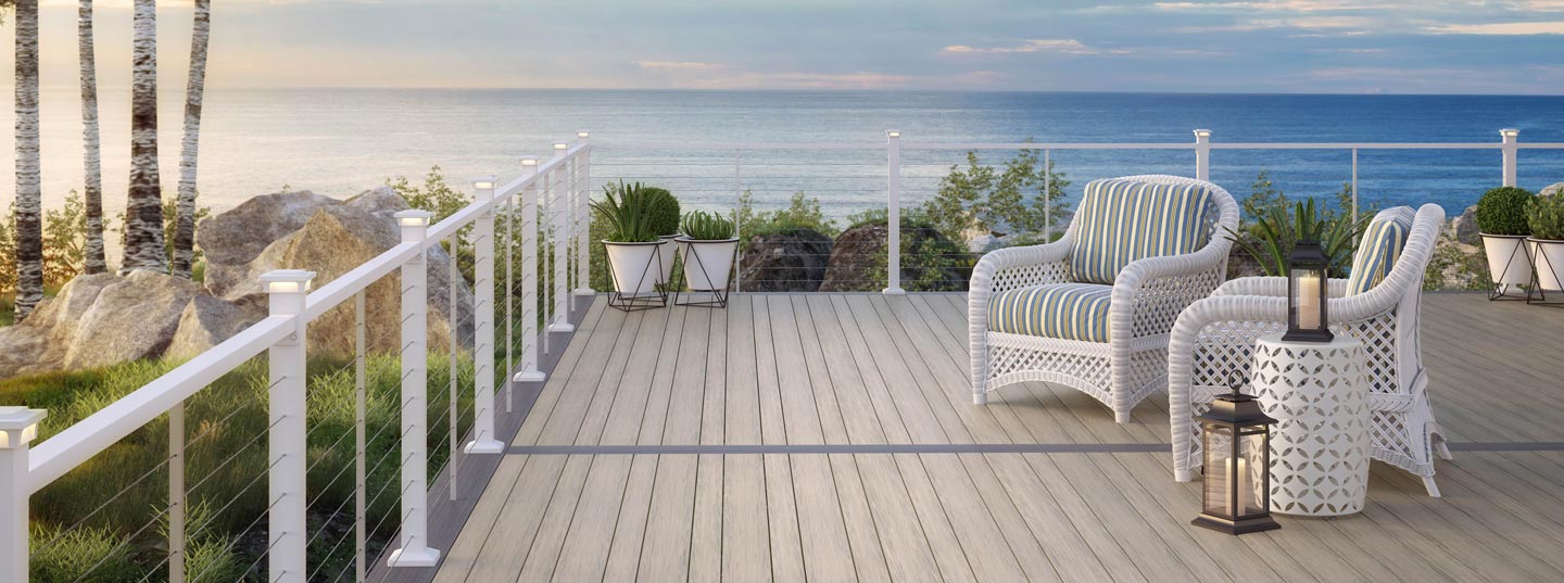 Grey deck with white railing and furniture, overlooking a body of water.