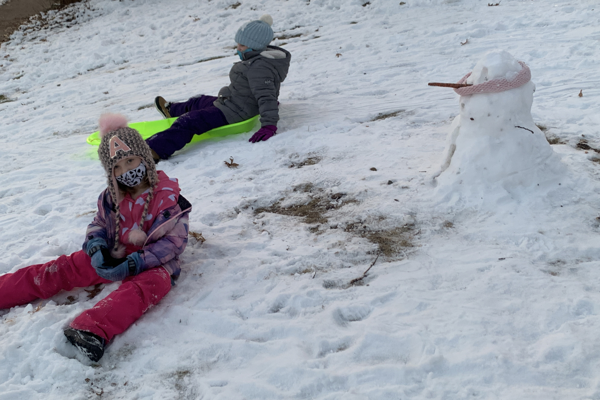  Two children playing in the snow near a snowman. 