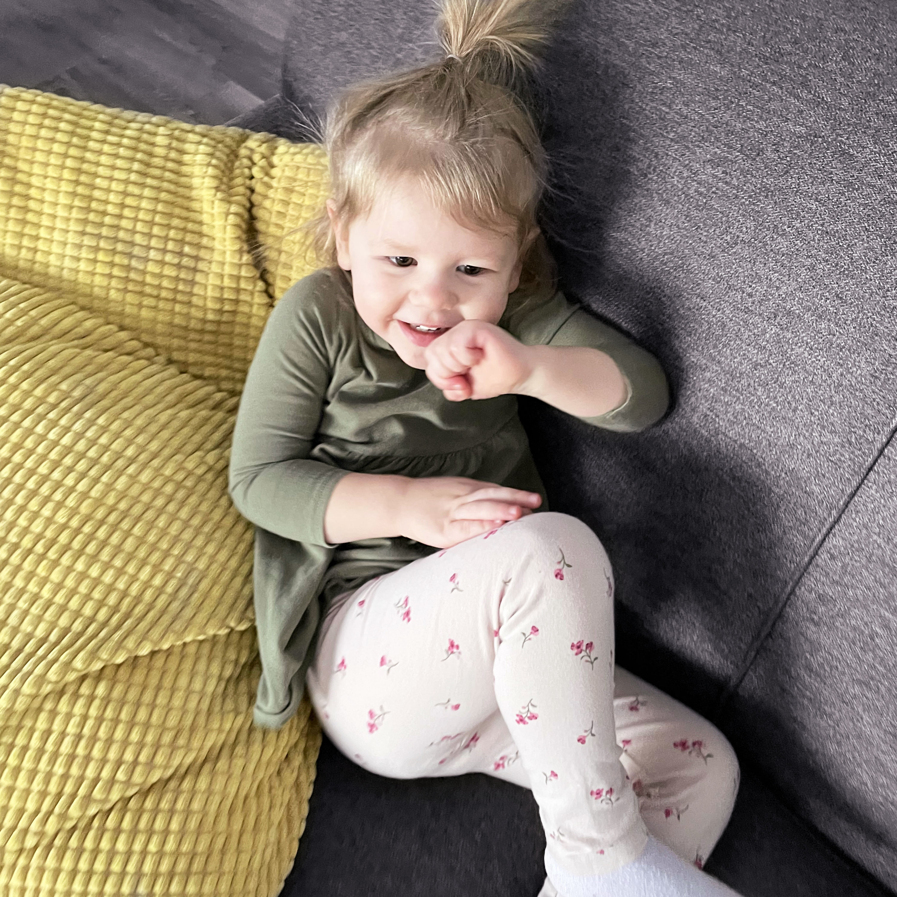 Smiling girl lying on a grey couch with a yellow pillow. 