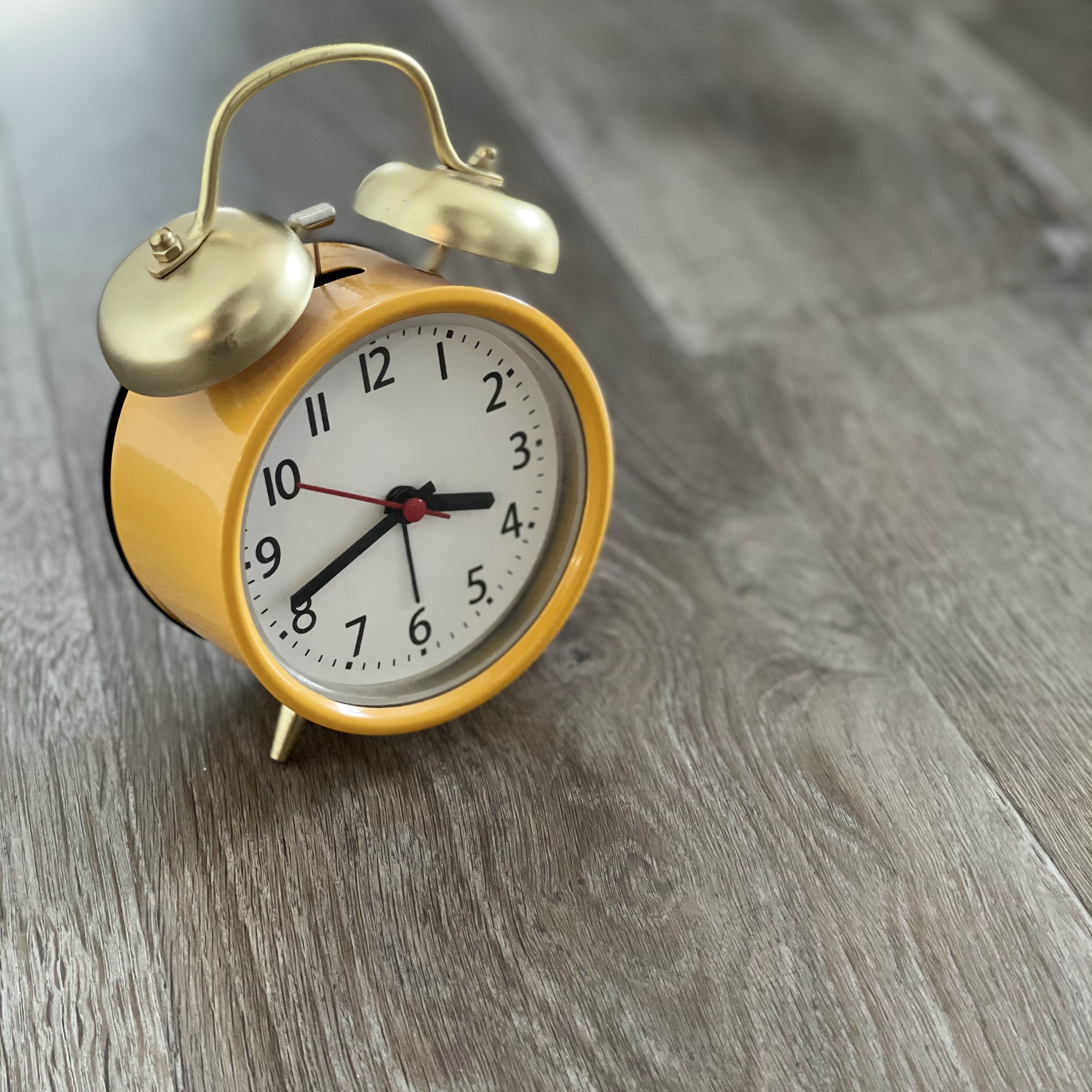 Yellow alarm clock sitting on a grey wood floor.