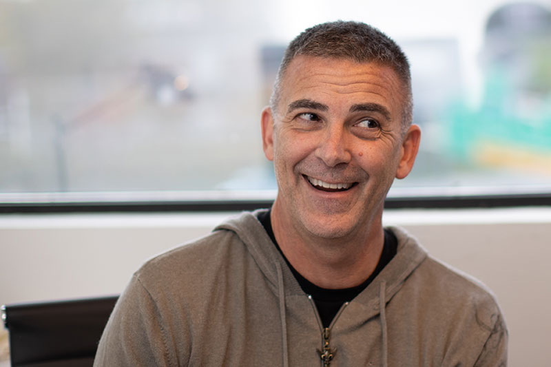 Man with zip-up sweatshirt smiling and looking to the side.