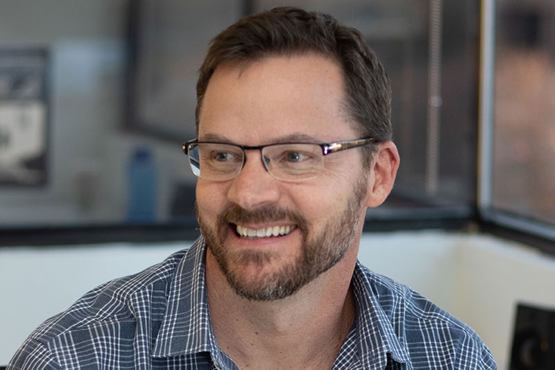 Man with glasses and beard smiling and looking to the side.