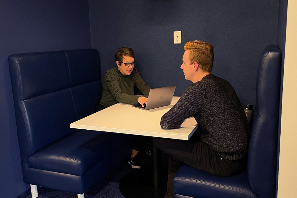 Two Anthologic employees sitting at a white table with navy blue booths. 
