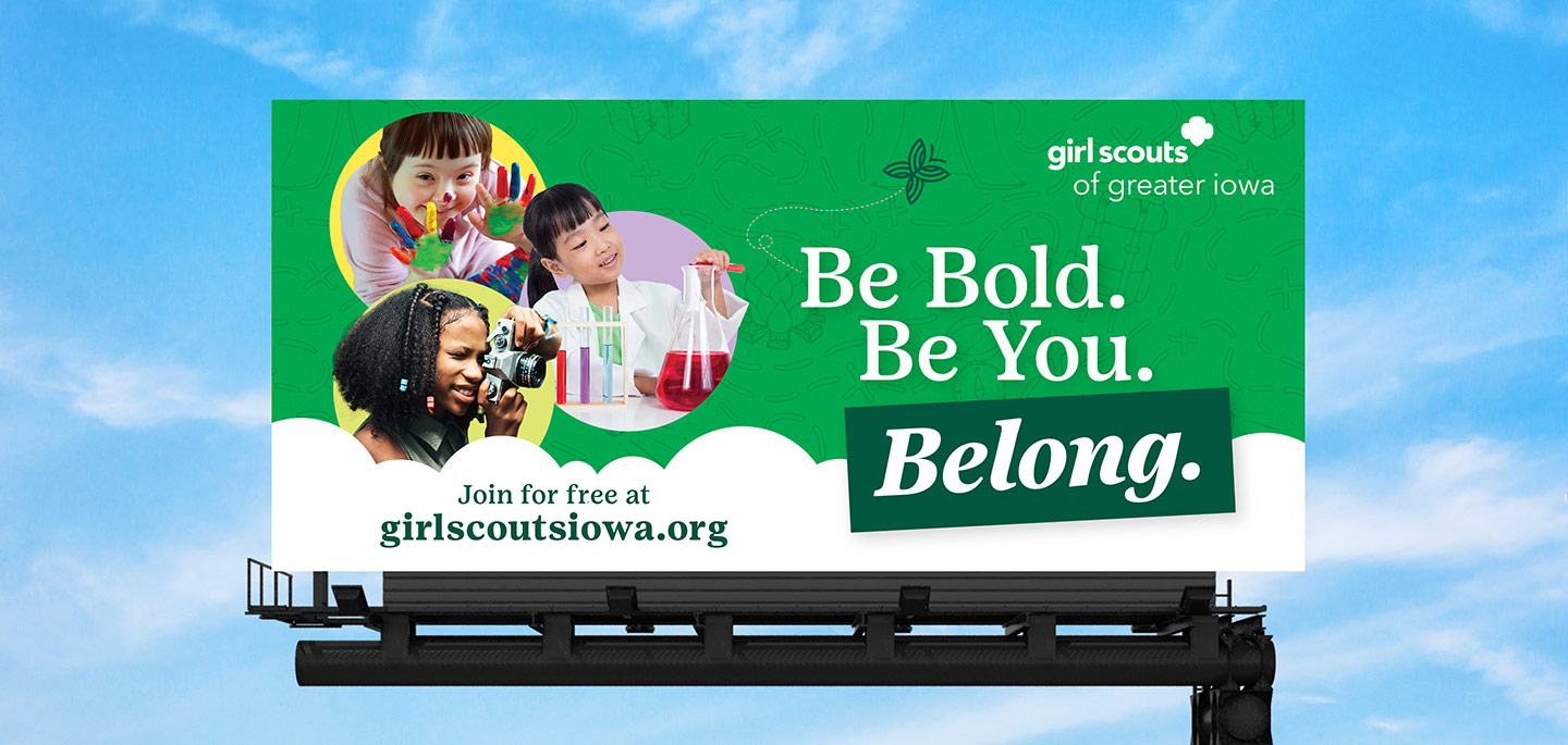 Billboard ad reading “Be Bold. Be You. Belong.” with a blue sky in the background.
