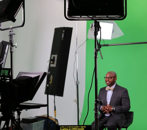 Presenter on a green-screen stage with teleprompter, lighting, and confidence monitor