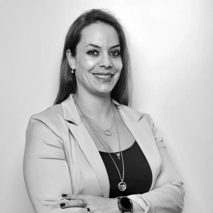 Foto de perfil Milena Hidalgo. Na foto se vê uma mulher de braços cruzados e sorriso no rosto.