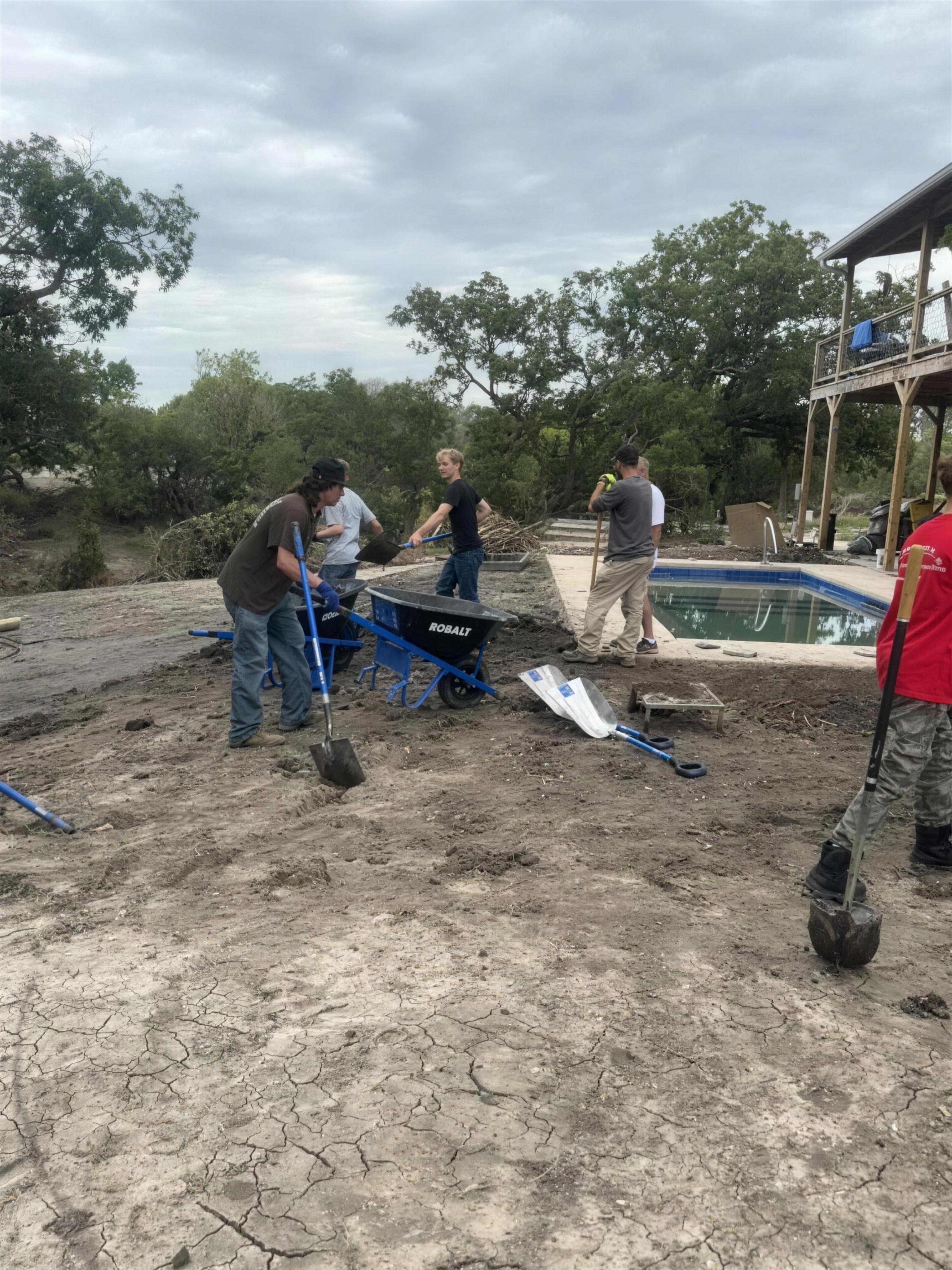 PCG team clearing mud beside a flood-filled swimming pool