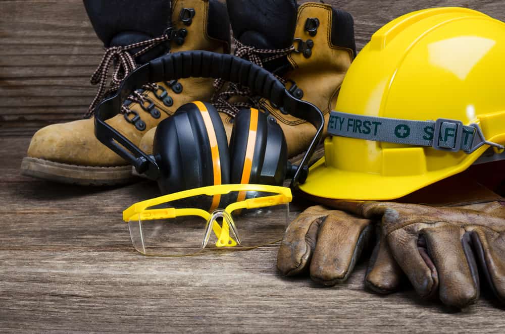 Construction shoes, glasses, ear muffs, gloves, and hard hat that says “safety first”