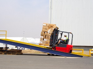 Forklift loaded with boxes slowly moving up a ramp to load a truck.