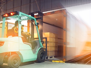 Forklift loading a pallet of boxes onto a truck from a loading dock.