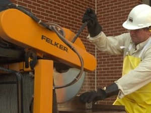 A worker wearing PPE operating a stationary masonry saw to cut pavers.