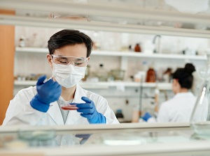 Lab worker wearing gloves, face mask and safety glasses.