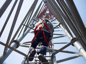 Worker wearing a hardhat and fall protection climbing up a tower.