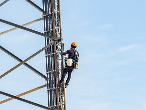 Worker wearing a hardhat and fall protection climbing up a tower.