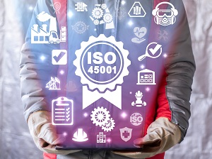 Worker wearing PPE holding a tablet that shows a graphic representation of ISO 45001 including safety icons.