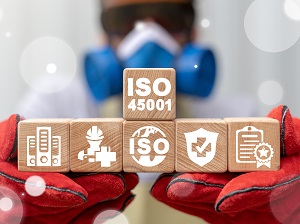 A worker in full PPE holding up building blocks that say ISO 45001 and have various safety graphics on them.