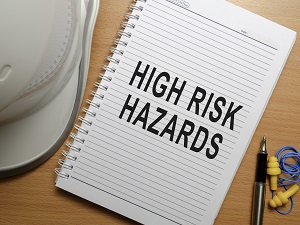 A notebook on a desk that reads "High Risk Hazards" with a hard hat and hearing protection nearby.