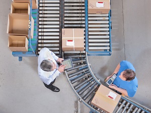 A supervisor and a worker standing near a conveyor system with boxes on it.