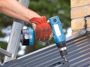 Worker standing on a ladder using a power tool to make repairs.