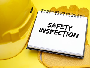 A yellow hard hat and yellow gloves with a notepad that says Safety Inspection.